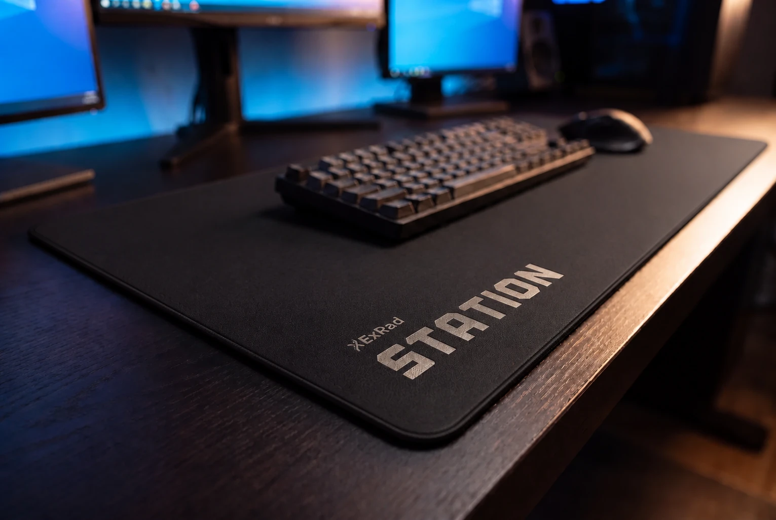 The ExRad Station wordmark on a matte-black full-width desk pad with a keyboard and mouse